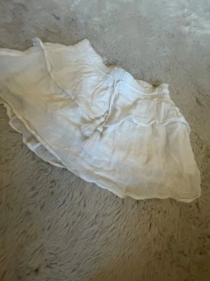 Vit volangkjol från Gina Tricot - Söt vit kjol från Gina Tricot med volangkant och resår i midjan. Den är lite missfärgad på insidan av solkräm som man ser på bild 2 därav priset men det syns inte då det är på insidan den är i storlek 146/152/xxs. Pris kan diskuteras och skriv för mer bilder
