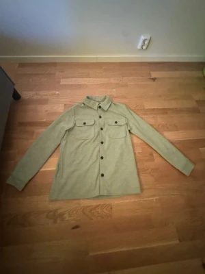 Grå  overshirt med fickor - Grå overshirt med två bröstfickor och svarta knappar. Mjuk och stilren modell med lång ärm. Bra skick och passar perfekt till både jeans och andra outfits. Storlek M.