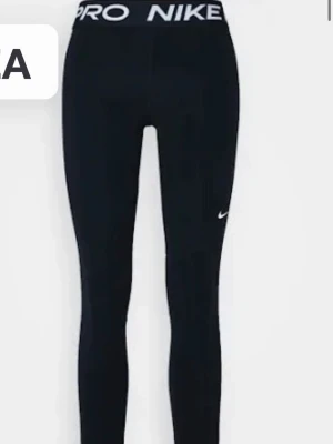 Svarta Nike Pro leggings - Snygga svarta Nike Pro leggings med Tight passform och diskret vit Nike-logga på benet. Perfekta för träning eller chill. Tillverkade i stretchigt material för maximal komfort.