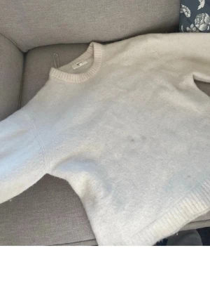 Vit stickad tröja från Gina Tricot - Mysig vit stickad tröja från Gina Tricot i ullblandning. Tröjan har rund halsringning och ribbade muddar vid ärmslut och nederkant. Perfekt för kalla dagar och enkel att matcha med olika outfits.