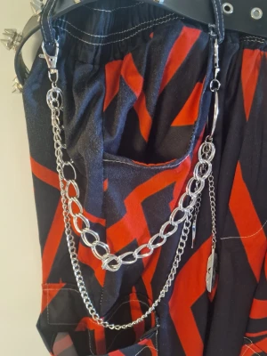 Byxkedja fjäder - Byxkedja fjäder. Innerkedja 47 cm. Ytterkedja 62 cm. Fjäderberlock 16 cm. Fyrkantigberlock 12,5 cm.