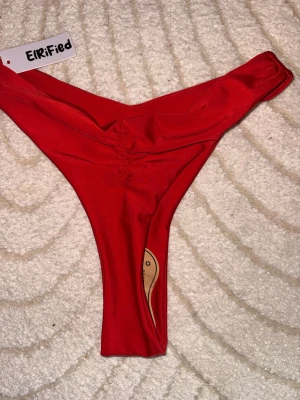 Röda bikiniunderdelar från Elrified - Snygga röda bikiniunderdelar från Elrified med hög skärning och scrunch-detalj bak. Tillverkade i ett mjukt och stretchigt material som sitter tight och bekvämt. Perfekta för sommarens strandhäng eller poolparty. Helt oanvänd. 