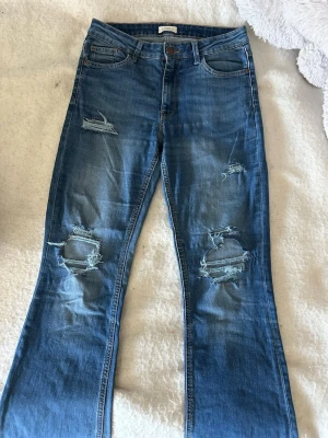 Blå slitna jeans från Lindex - Ett par blå jeans från Lindex med snygga slitningar och hål på båda benen. Jeansen har klassisk femficksmodell, lite högre midja och utsvänga ben!💖💖💖