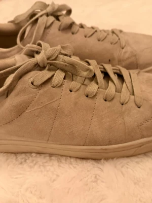 Beige mockasneakers med snörning - Stilrena sneakers i beige mocka med matchande snörning och låg profil. Skorna har en enkel och clean design utan synliga loggor, perfekt för en avslappnad och trendig look. Yttermaterialet är mocka och sulan är i gummi.