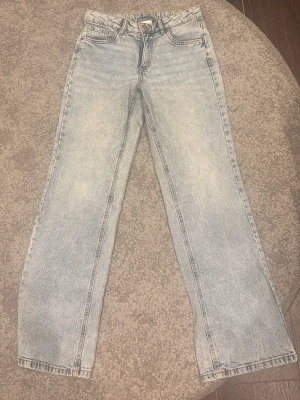 Ljusblå raka jeans med fickdetaljer - Säljer ett par ljusblå jeans med raka ben och klassisk femficksmodell. Jeansen har snygga ficklock med knapp bak och en avslappnad passform. Tillverkade i denim med en tvättad look som ger en cool vintagekänsla. Storlek 164 men får även som xs-s