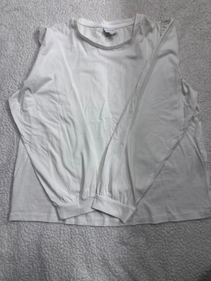 Vit långärmad topp med puffärm - En enkel och stilren vit långärmad topp med lätt puff vid axlarna. Tillverkad i mjukt bomullstyg som känns skönt mot huden. Perfekt att matcha med jeans eller kjol för en clean look. Den är liten i storleken.