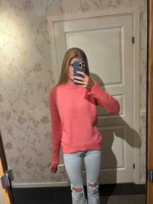 Rosa stickad tröja med rund hals - En söt rosa stickad tröja med rund hals och långa ärmar. Tröjan har en enkel och stilren design med ribbstickade muddar vid ärmslut och nederkant. Perfekt för att hålla sig varm och snygg under kyligare dagar. Bara använd en gång så den är i väldigt bra skick.