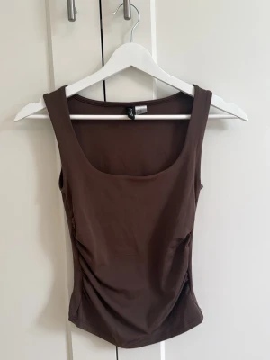 Linne från H&M - Snygg brunt linne med breda axelband och rundad urringning. Toppen har en figurnära passform och är tillverkad i ett mjukt, stretchigt material. Köpt på H&M och aldrig använd så är precis som ny💗
