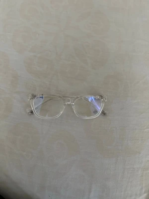 Chrome hearts - Säljer ett par trendiga solglasögon med transparent, rektangulär båge i syntetmaterial. Glasen är också klara vilket ger en modern och clean look. Perfekta för dig som vill ha en stilren accessoar som sticker ut.