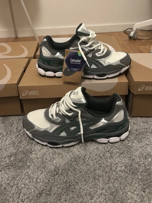 ASICS gråvita sneakers med mesh - Snygga sneakers från ASICS i grått och vitt med detaljer i silver. Ovandelen är i mesh och syntet för bra andningsförmåga. Skorna har Ortholite-innersula för extra komfort och en chunky vit sula. Perfekta för dig som gillar sportig stil.