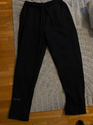 Syna world byxor - Svarta mjukisbyxor från Forgive Me med broderad logga på vänster ben. Byxorna har dragsko i midjan, raka ben och dragkedjor vid bensluten. Perfekta för chill dagar eller när du vill ha en avslappnad stil.