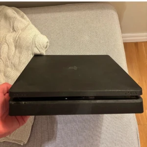 Svart PlayStation 4 Slim konsol - Säljer en svart PlayStation 4 Slim konsol med stilren och kompakt design. Konsolen har en matt finish och är tillverkad i plast. Perfekt för gaming och underhållning hemma. En kontroll och alla sladdar du behöver följer med