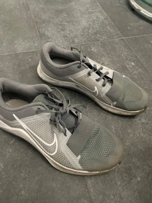 Grå Nike sneakers med meshdetaljer - Snygga grå sneakers från Nike med vit swoosh på sidan. Skorna har meshpaneler för extra ventilation, snörning och bred resårdetalj över foten. Yttersulan är mönstrad för bra grepp och skon har en sportig, modern look.