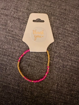 Armband med rosa och guldiga pärlor - Säljer ett färgglatt armband med små pärlor i rosa och guld. Armbandet är elastiskt och passar de flesta handleder. Perfekt för dig som vill addera lite färg till din stil!