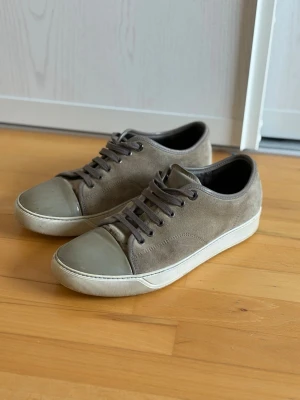 Gråa sneakers med mocka och gummitå. Priset kan diskuteras! - Säljer ett par stilrena gråa sneakers i mocka med matchande grå gummitå och vita sulor. Skorna har klassisk låg profil, grå snörning och en enkel design som passar till det mesta. Perfekta för dig som gillar en clean och avslappnad look.