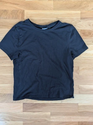 Svart basic t-shirt i bomull - En enkel svart t-shirt i mjuk bomull med rund hals och korta ärmar. Perfekt till jeans eller shorts för en clean och avslappnad stil. Klassisk passform och utan tryck eller mönster.
