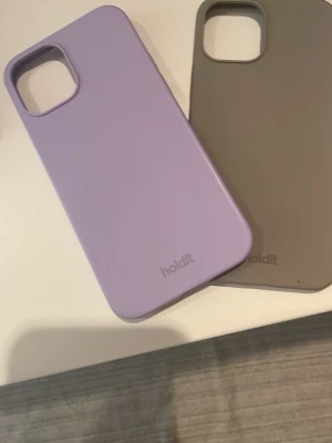Två mobilskal från Holdit, lila & beige - Säljer två snygga mobilskal från Holdit, ett i ljuslila och ett i beige. Båda har en stilren, matt finish och är gjorda i mjukt silikon som ger bra grepp. Perfekt för dig som vill skydda mobilen med stil.
