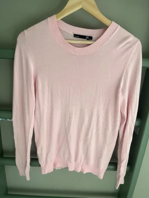 Ljusrosa stickad tröja 157 - Söt ljusrosa stickad tröja från 157 med rund halsringning och ribbade muddar vid ärmslut och nederkant. Tröjan har en enkel och clean design som passar perfekt till många olika outfits. Materialet känns mjukt och bekvämt mot huden.
