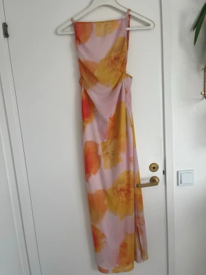 Lång blommig klänning med smala band - Säljer en lång klänning (storlek S men jag själv brukar ha XXS-S i klänningar) med smala axelband och blommigt mönster i gula och orange toner på ljusrosa botten. Klänningen har en rak siluett och är perfekt för sommarens alla tillfällen. Materialet känns lätt och svalt. 
