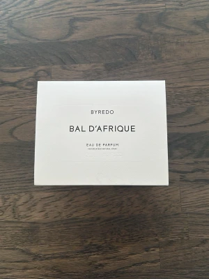 Byredo Bal d'Afrique Eau de Parfum - Byredo Bal d'Afrique Eau de Parfum i elegant vit kartong med stilren svart text. Förpackningen har en lyxig känsla och parfymen är känd för sin unika doftprofil inspirerad av afrikanska influenser. Perfekt för dig som gillar exklusiva dofter.