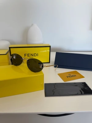 Fendi runda solglasögon i guld - Säljer ett par lyxiga solglasögon från Fendi med runda, mörka linser och tunna guldfärgade bågar. På både linsen sitter en glittrig Fendi-logga i hörnet. Kommer med originalfodral, putsduk och certifikat. OBS! Ej verifierat om de är äkta.
