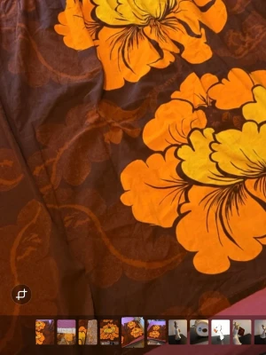 Retro gardiner med stora blommor - 2 stycken Bruna gardiner i bomull med stora, färgstarka blommor i orange och gult. Mönstret är inspirerat av 70-talet och ger en vintagekänsla till sovrummet. Perfekt för dig som gillar unika och retro detaljer i inredningen.