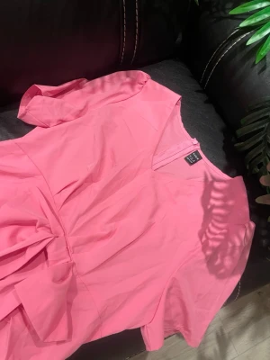 Rosa klänning med knytband i midjan - Supersöt rosa klänning med korta ärmar och v-ringning. Klänningen har ett knytband i midjan som ger en fin siluett och ett enkelt, stilrent uttryck. Perfekt för dig som vill ha en färgklick i garderoben!
