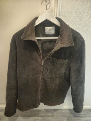 Brun manchester overshirt från Bläck - Snygg brun overshirt i manchestertyg från Bläck. Jackan har dragkedja framtill, en bröstficka och klassisk krage. Perfekt lager på lager-plagg med avslappnad passform och trendig retrostil.
