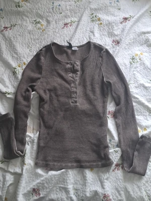 Brun ribbad långärmad tröja XS - Säljer en brun ribbad långärmad tröja från H&M:s DIVIDED-kollektion. Tröjan har knappar framtill vid halsen och är tillverkad i ett mjukt, stretchigt material.