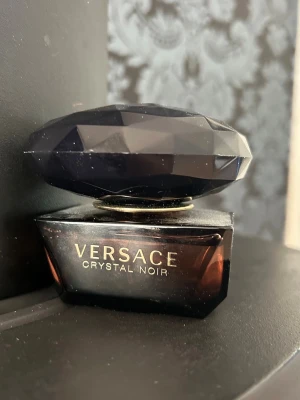 Versace Crystal Noir parfym - Versace Crystal Noir parfym i en elegant mörklila glasflaska med facettslipat svart lock. Flaskan har en lyxig och unik form som verkligen sticker ut på parfymhyllan. Perfekt för dig som gillar exklusiva dofter och snygg design. Använd max 3 gånger. 
