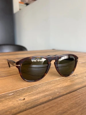 Bruna solglasögon med rundad form - Snygga solglasögon med brunsköldpaddsmönstrad båge och rundade linser. Klassisk design med metalliga detaljer vid gångjärnen och mörka glas. Perfekta för att höja din stil på soliga dagar.