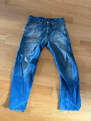 Levi's Engineered Jeans blå 31 - Säljer ett par Levi's Engineered Jeans i klassisk blå denim med slitningar och raka ben. Jeansen har fem fickor, knappgylf och tydliga kontrastsömmar. Perfekta för dig som gillar en avslappnad och tidlös stil. Storlek: 32/32
