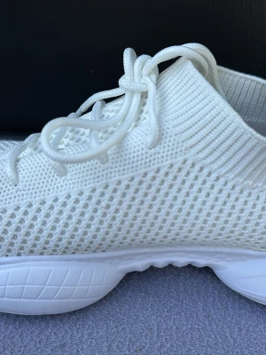 Vita stickade sneakers med snörning - Snygga vita sneakers med stickad ovandel och snörning. Skorna har en chunky sula och ventilerande meshmaterial som ger en sportig och modern look. Perfekta för dig som gillar stilrena och bekväma skor till vardags.