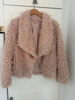 Teddyjacka från Esprit - Säljer en fluffig och trendig rosa teddyjacka från Esprit. Jackan har stora slag, mjukt foder och en oversized look. Perfekt för dig som vill ha en mysig och stylish jacka med cool textur. Materialet är syntetiskt och jackan har långa ärmar.