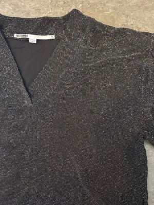 Glittrig svart topp från Just Female - Snygg svart topp från Just Female med glittriga detaljer och v-ringning. Perfekt för dig som vill sticka ut lite extra. Materialet känns mjukt och följsamt mot huden. Toppen har en klassisk passform och passar till många olika stilar.