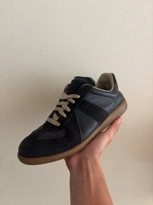 Maison Margiela Skor  - Snygga mörkblåa sneakers med beige snören och gummisula. Skon har en mix av mocka och slätt läder, samt en låg silhuett som ger en clean look. (( förekommer skador tex ens snöret har gått av men de funkar att använda )) 