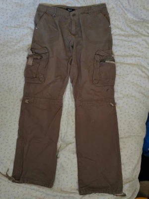 D&G / Dolce & Gabbana bruna cargopants  - Säljer ett par bruna cargobyxor från D&G med flera stora fickor på benen och detaljerade sömmar. Byxorna har raka ben och dragkedjor på fickorna för extra funktionalitet. Perfekta för en avslappnad och cool stil.