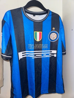 Inter Milan Milito matchtröja XL - Säljer en blå och svart randig matchtröja med Milito och nummer 22 på ryggen. Tröjan har klubbmärke, Champions League-märke på ärmen och tryck från finalen i Madrid 2010. 