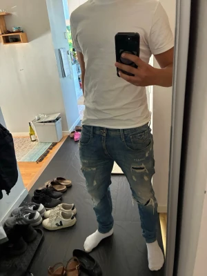 Blå slitna jeans med hål - Säljer ett par blå jeans med flera slitningar och hål på benen för en riktigt avslappnad och trendig look. Jeansen har en rak passform och klassisk femficksdesign. Perfekta för dig som gillar en edgy stil🔥