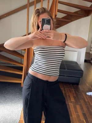 Randig bandeau tubtopp - Säljer en stilren bandeau tubtopp med svartvita ränder. Toppen är ärmlös och axelbandslös, perfekt för varma dagar. Materialet känns mjukt och stretchigt, vilket gör den bekväm att bära. Passar till både jeans och kjol för en trendig look 💝