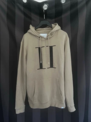 Les deux hoodie - Snygg beige hoodie med stor svart romersk siffra II på bröstet. Hoodien har huva med dragsko och en klassisk magficka framtill. Tillverkad i mjukt material som känns skönt mot huden. Perfekt för en avslappnad och trendig look. Jätte bra kvalité och använd två gånger. Hör av er vid frågor eller prisförslag!