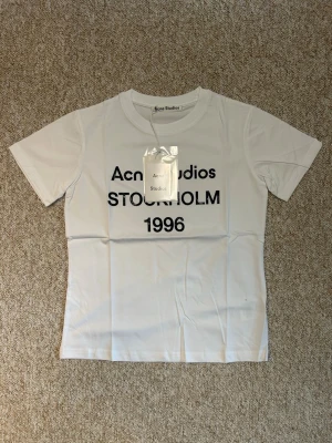 Vit S Acne Studios t-shirt  - Vit t-shirt från Acne Studios med trycket 'Acne Studios STOCKHOLM 1996' på bröstet. Klassisk passform och rund hals. Perfekt basplagg för en clean och stilren look.OBS: osäker på äktheten då jag köpte den av en kompis, därför det låga priset (449kr ist för ca 2000-3000kr) Tveka inte att skriva om du har några funderingar!