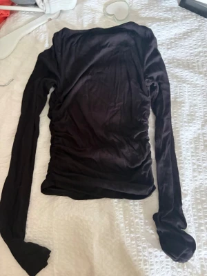 Svart långärmad topp med snörning - Säljer en svart långärmad topp med snygg snörning i sidorna som ger en cool rynkad effekt. Toppen har en tight passform och är gjord i mjukt stretchigt material, perfekt att styla till jeans eller kjol.