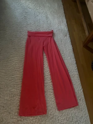 Yoga pants i korall - Säljer ett par yogabyxor i en snygg rosa färg med breda ben och hög, vikbar midja. Byxorna har en avslappnad passform och är gjorda i ett mjukt, stretchigt material som känns skönt mot huden. Perfekta för chill dagar eller när du vill vara extra bekväm.