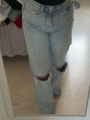 Gina Jeans - Säljer ett par ljusblå jeans med raka ben och stora slitningar vid knäna. Jeansen är hög midjade