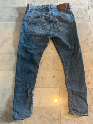 512 Levis - Klassiska blå jeans med rak passform och två bakfickor. Jeansen har en läderpatch i midjan och en liten röd etikett på ena bakfickan. Tillverkade i denim med en tidlös look som passar till det mesta.