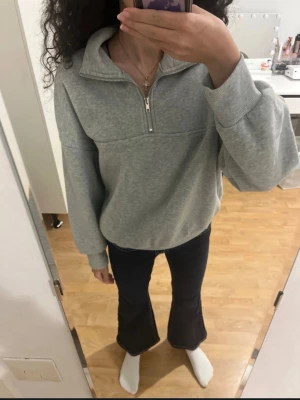 Grå oversized hoodie med half zip - Säljer en grå oversized hoodie med half zip och hög krage. Hoodien har långa ärmar och breda muddar vid ärmslut och nederkant. Perfekt för en chill och avslappnad stil. Materialet känns mjukt och skönt, troligen bomull eller polyester.