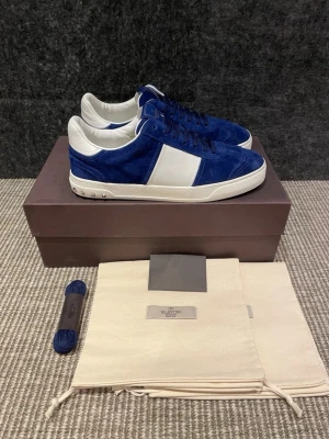 Valentino Flycrew - Snygga sneakers från Valentino i blå mocka med vita detaljer och vita sulor. Skorna har blå skosnören och en klassisk låg profil. Perfekta för dig som vill ha en stilren och exklusiv look. Skorna är endast använda ett fåtal gånger. Allt OG medföljer. Kontakta endast vid seriöst intresse.