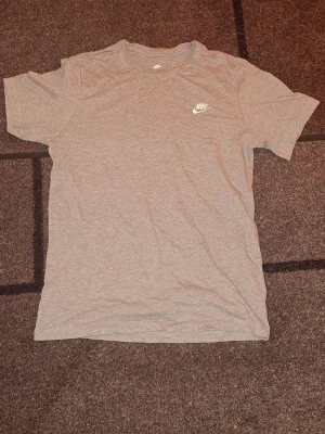 Grå t-shirt från Nike size M PRIS kan diskuteras! - Säljer en enkel och stilren grå t-shirt från Nike med klassisk logga på bröstet. T-shirten har rund halsringning och korta ärmar. Perfekt till vardags för en clean och sportig look. PRIS KAN DISKUTERAS size M.