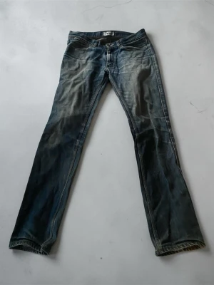 Blå raka jeans från Acne Studios - Säljer ett par klassiska blå jeans från Acne med rak passform och snyggt slitna detaljer. Jeansen har fem fickor, knappgylf och är tillverkade i robust denim. Perfekta för dig som gillar en avslappnad och tidlös stil.